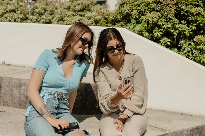 to unge damer ser på mobilen i solen ute